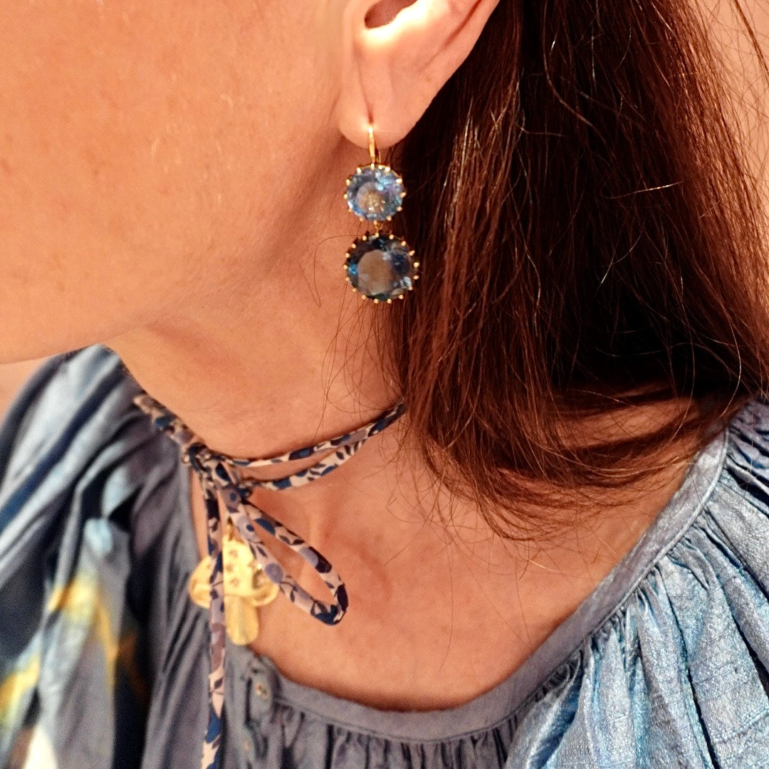 Close-up of a person wearing blue gemstone earrings with a blurred background