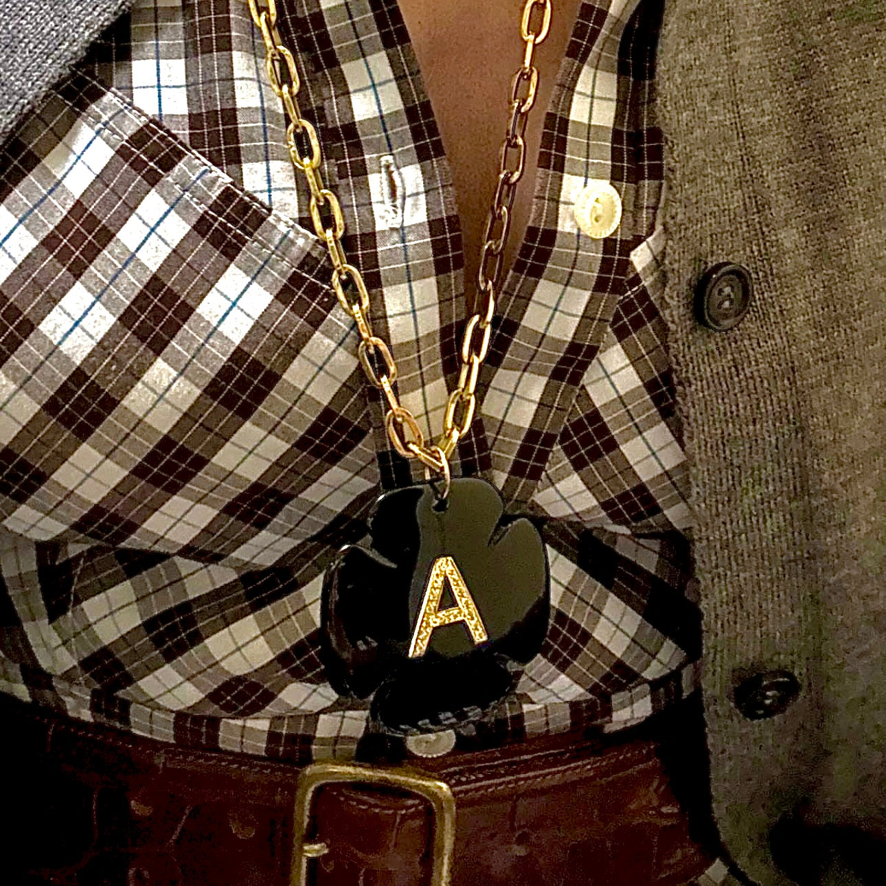 Person wearing a gold chain necklace with a black heart pendant featuring the letter 'A'.