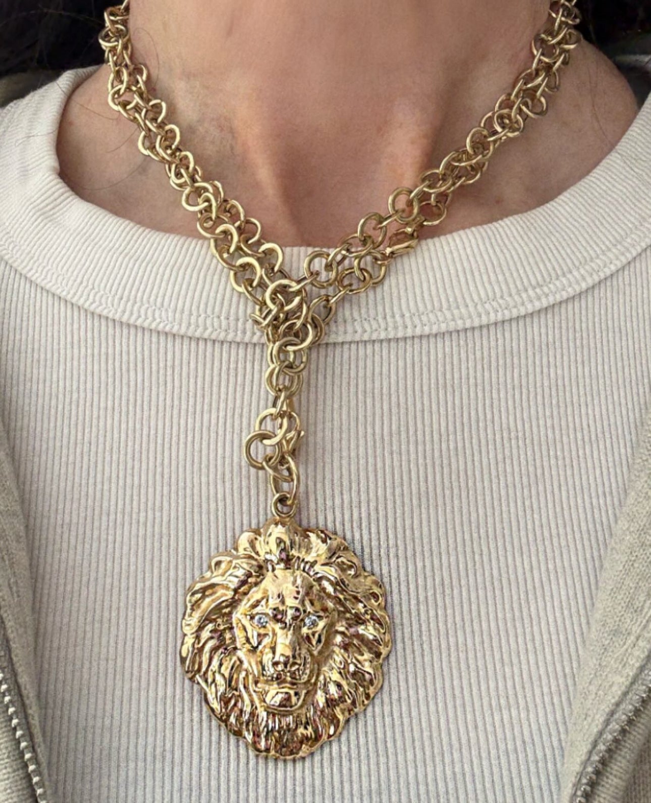 Gold chain necklace with a lion head pendant worn by a person.