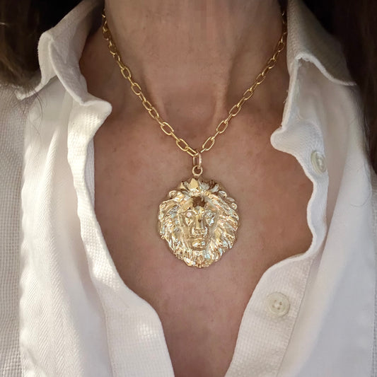 Gold necklace with a lion pendant worn by a person in a white shirt.