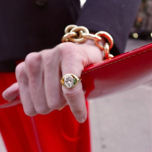Hand wearing a gold ring holding a red handbag with a blurred background