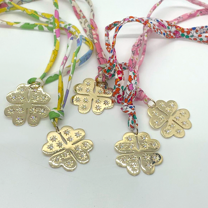 Gold four-leaf clover pendants on colorful braided cords against a white background
