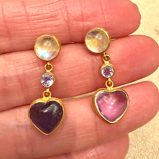 Heart-shaped gemstone earrings with gold accents held between fingers.
