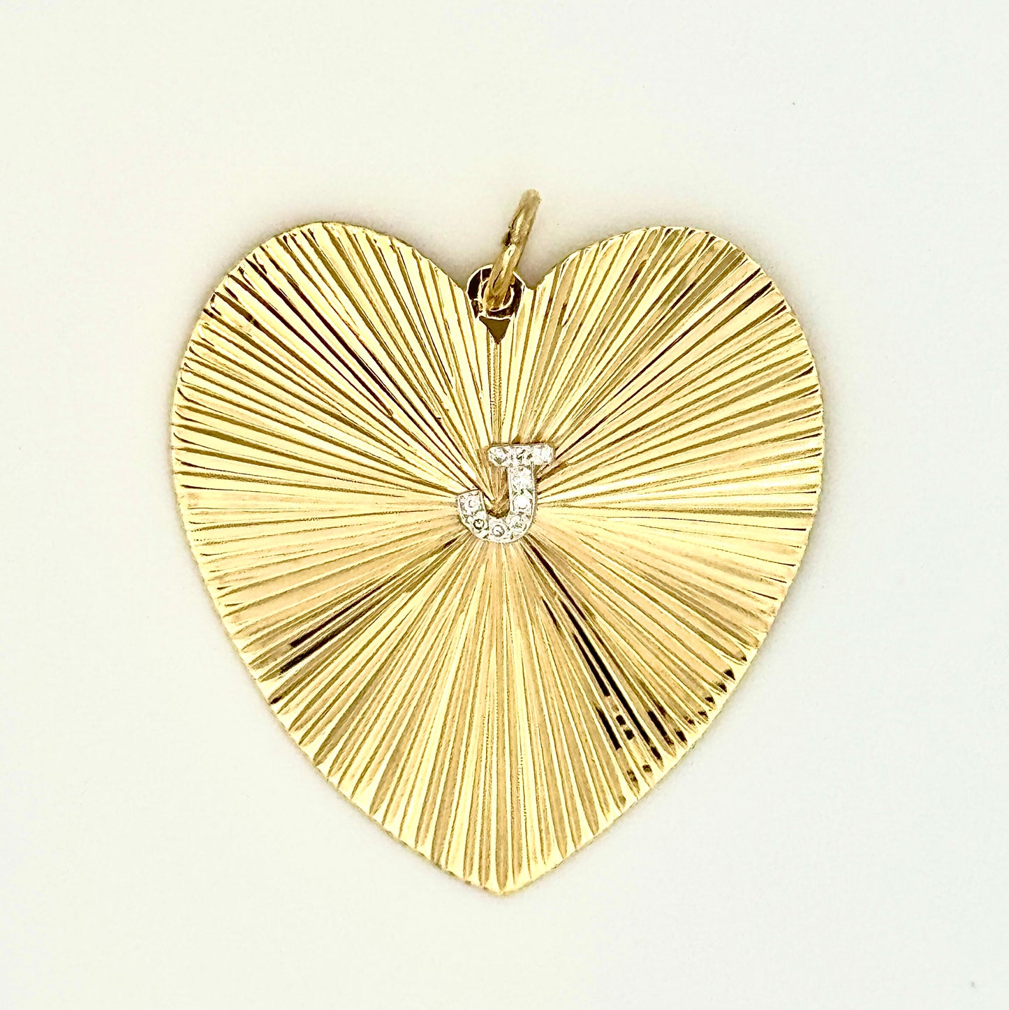 Gold heart-shaped pendant, etched radiating surface, with 'J' in diamonds in the center.
