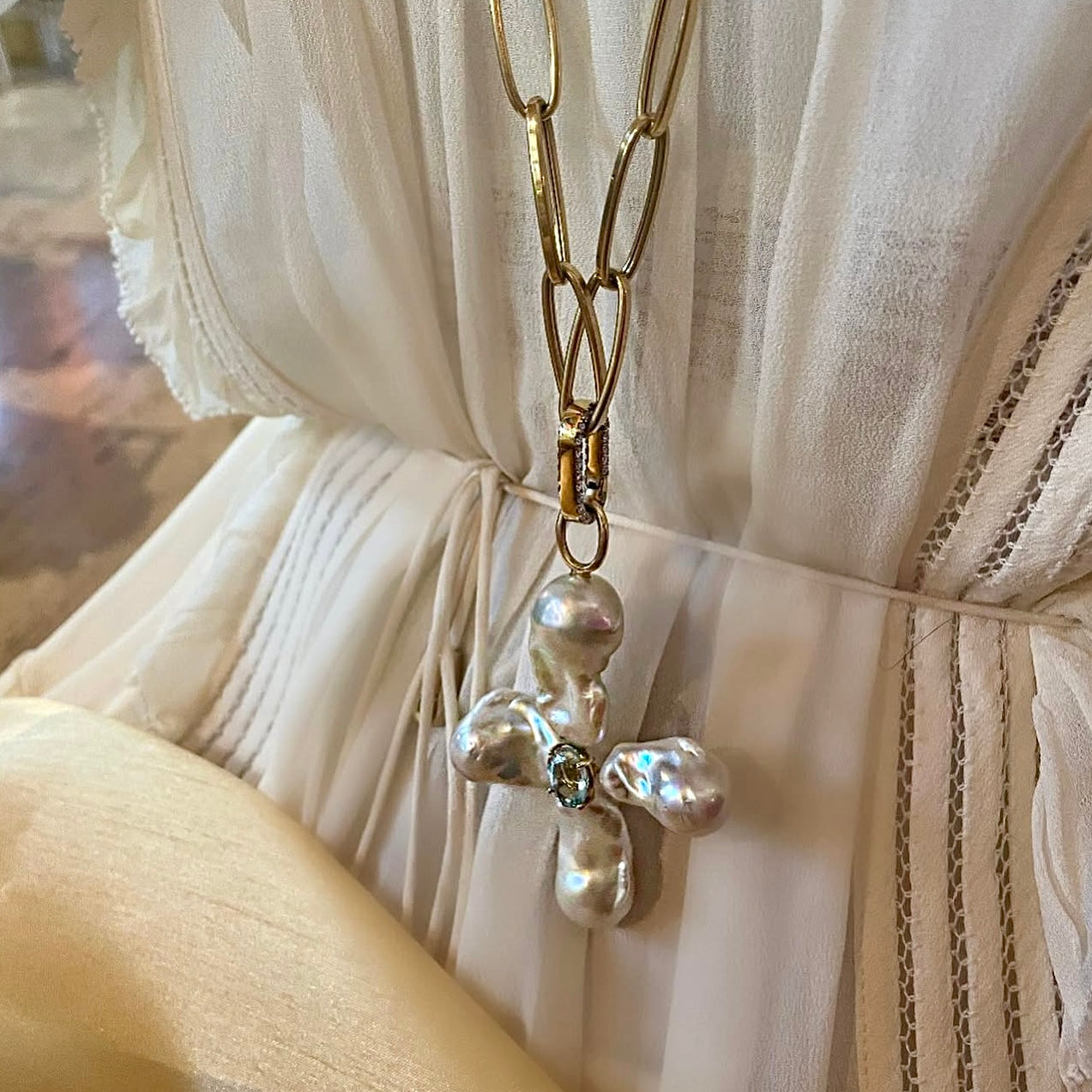 Gold necklace with a pearl pendant worn over a white dress.