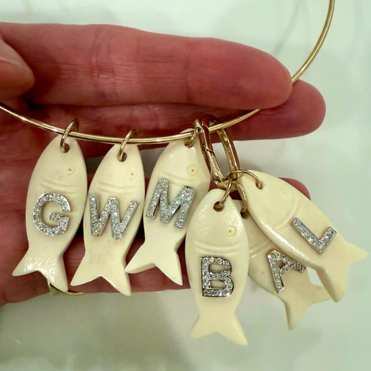 Gold bracelet with fish-shaped charms featuring initials held by a hand.