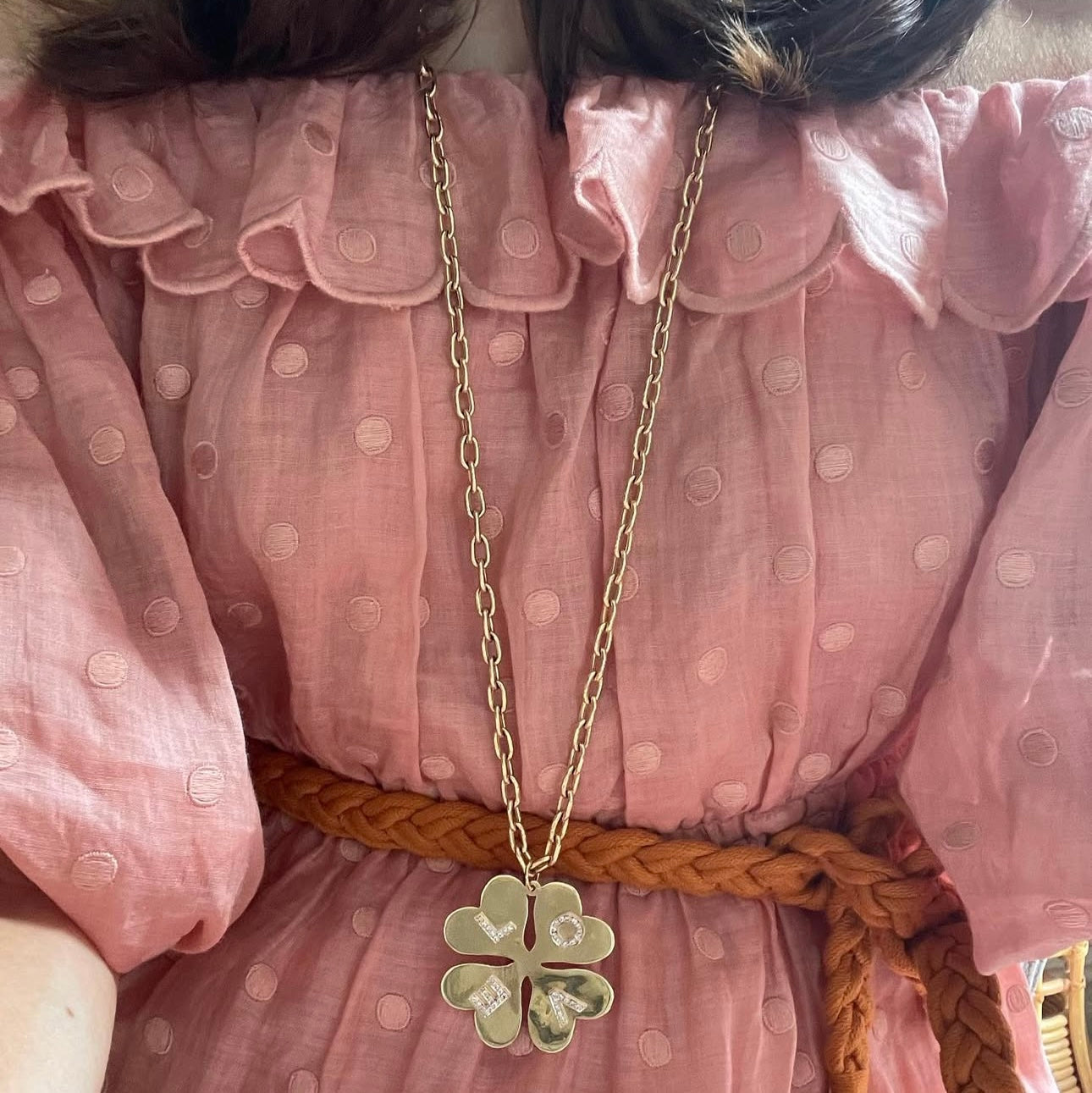 Person wearing a pink polka dot dress with a gold necklace and green pendant.