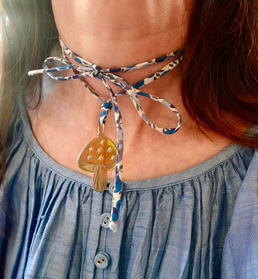 Person wearing mushroom shaped gold pendant on a blue, colorful cord wearing a blue dress.