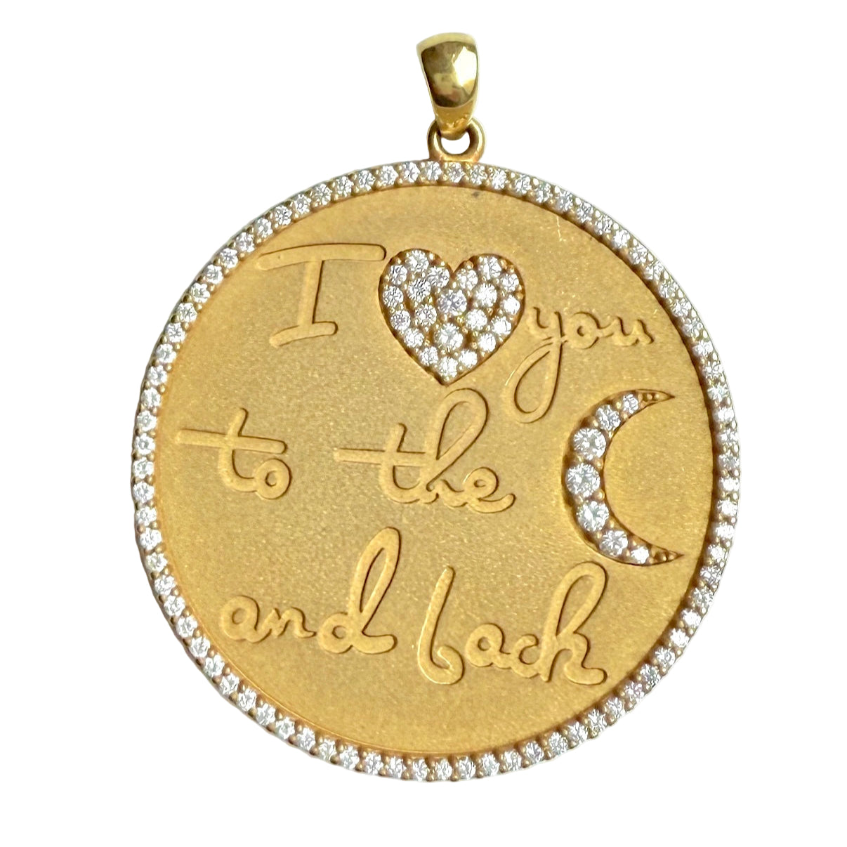 A round gold pendant that says "I love you to the moon and back" with a heart symbol set with diamonds instead of the word "love" and a crescent moon symbol set with diamonds instead of the word "moon". Gold pendant has a circle of close-set pave diamonds around its diameter.