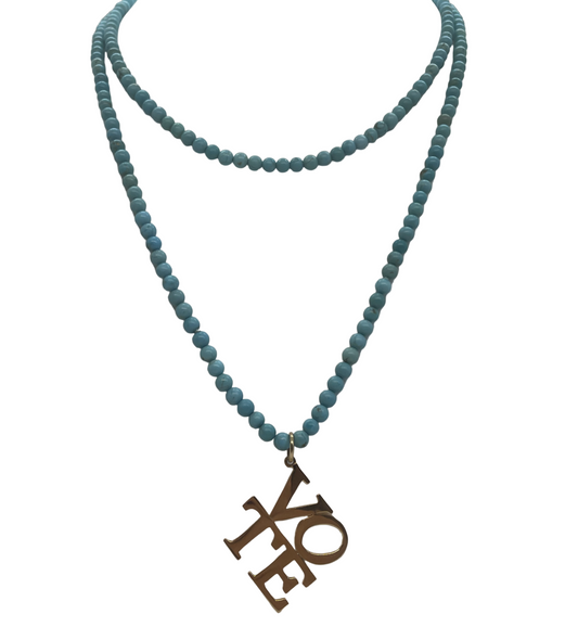 A turquoise beaded necklace displayed on a mannequin. The necklace features uniform beads and includes a charm/pendant.