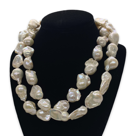A necklace of long, baroque-style white pearls displayed on a mannequin bust.