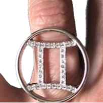 A hand holding a gold zodiac ring with pave diamonds on a finger.