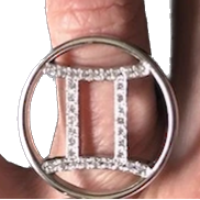 A hand holding a gold zodiac ring with pave diamonds on a finger.