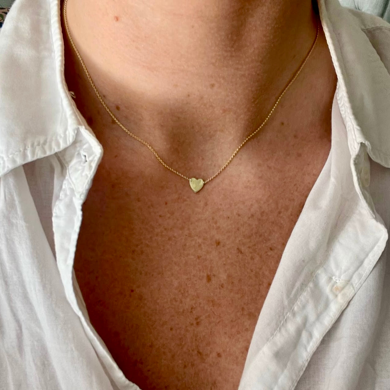 Gold necklace with a heart pendant worn by a person in a white shirt.