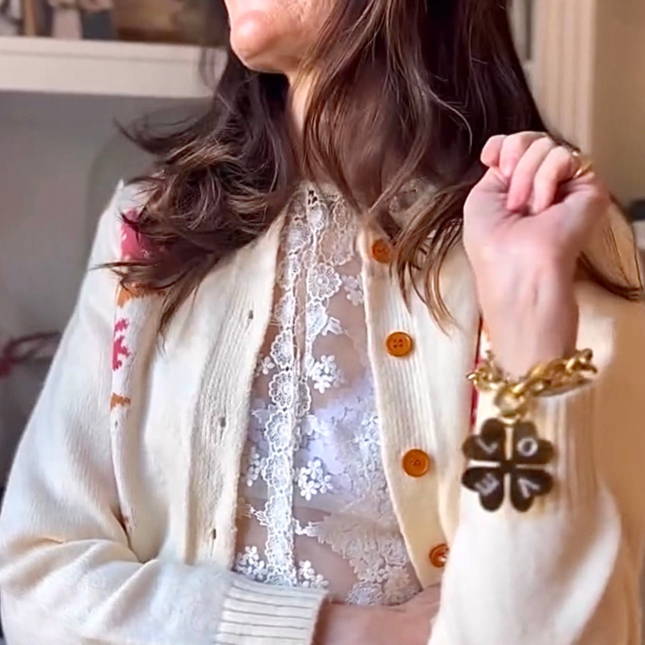 Close-up of a person wearing a white lace top and beige cardigan with floral patterns.
