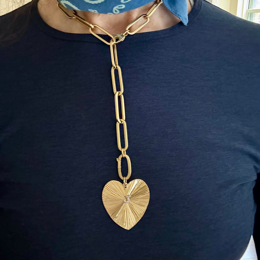 Gold chain necklace with a heart pendant worn by a person on a dark blue shirt.