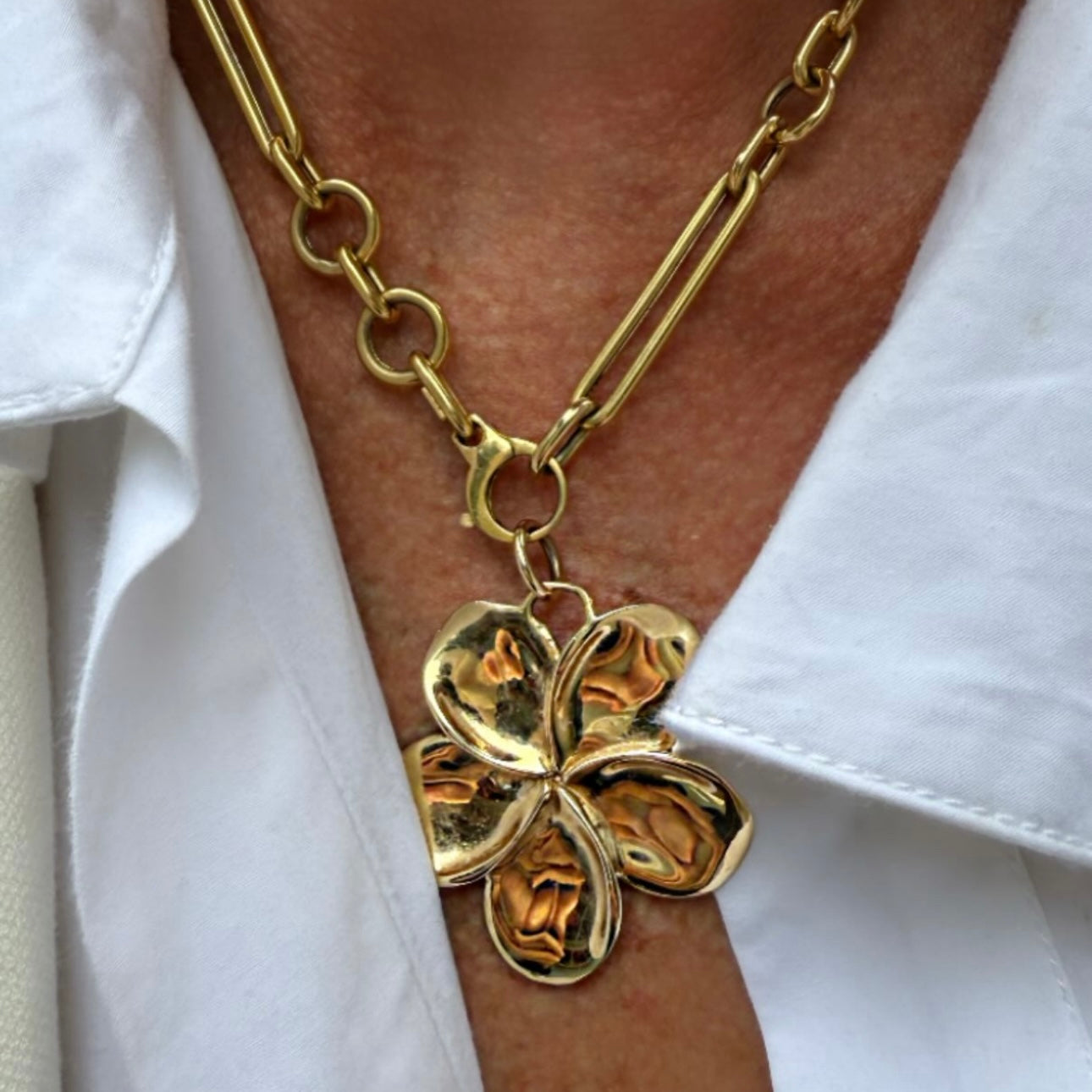Gold chain necklace with a flower-shaped pendant on a white shirt.