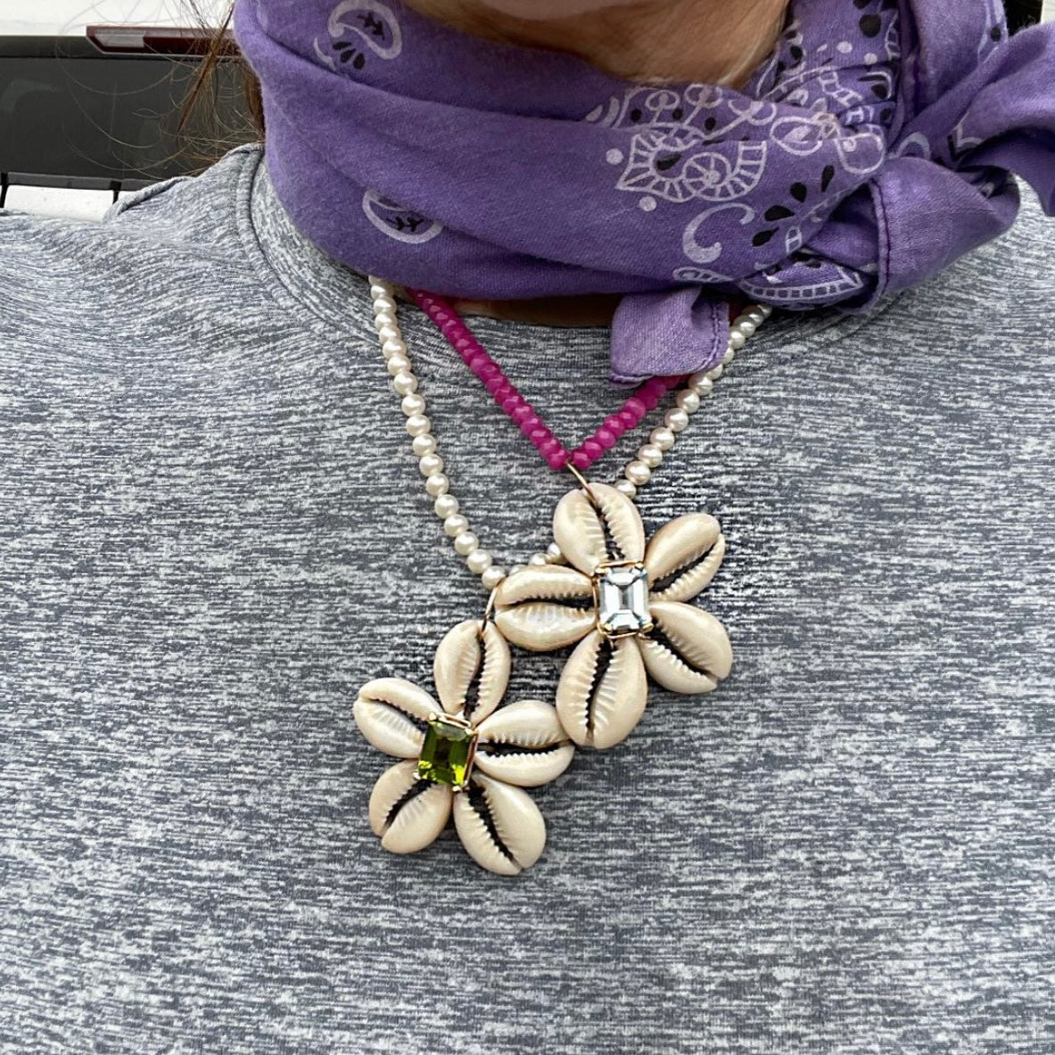 Necklace with floral pendants and a central gemstone worn by a person with a purple headscarf.