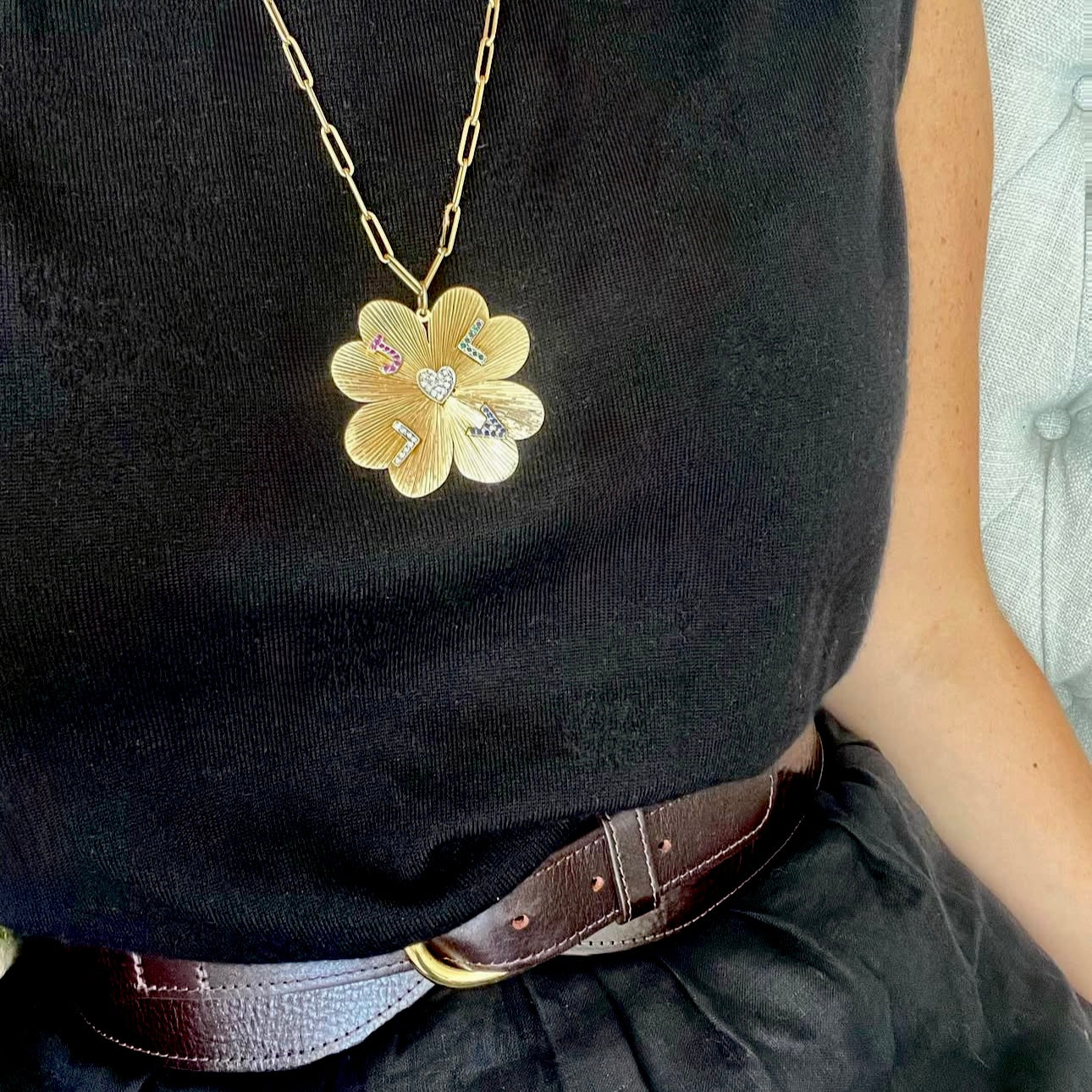 Person wearing a black top with a gold flower-shaped pendant necklace.