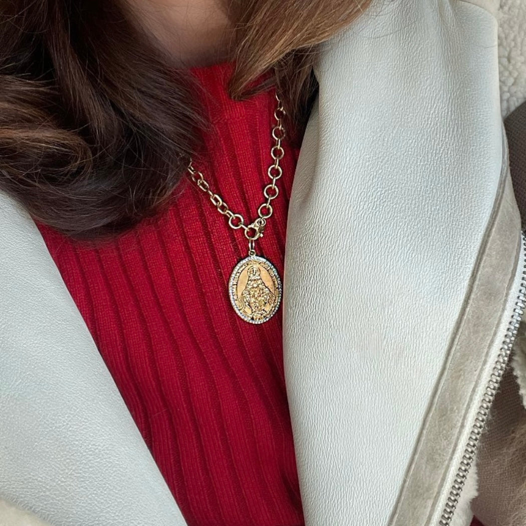 Person wearing a gold necklace with a pendant, red sweater, and white coat.