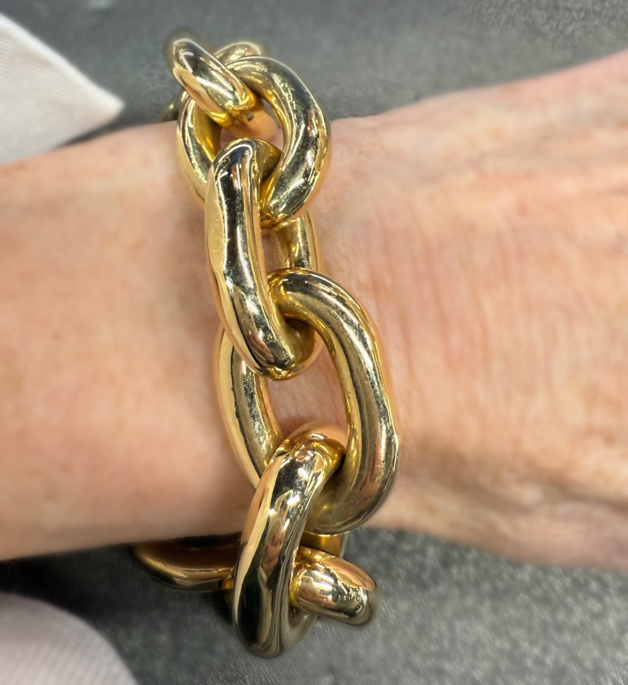 Gold chain bracelet on a wrist against a neutral background