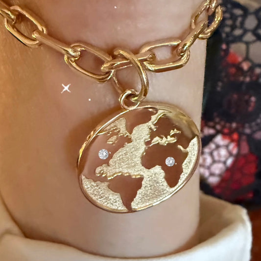 Gold chain bracelet with a world map charm on a wrist.