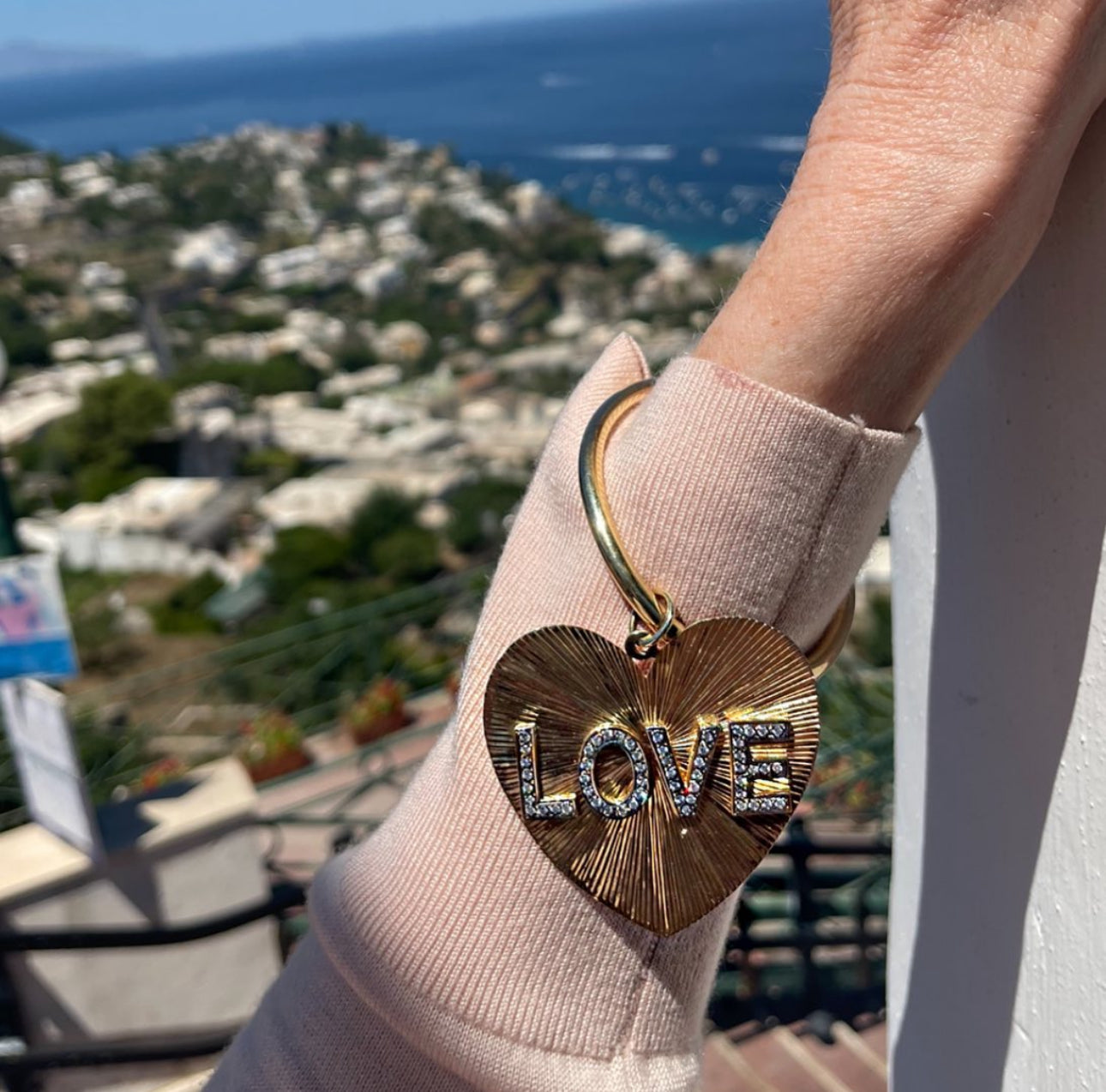 Heart-shaped keychain with 'LOVE' on a hand against a scenic background