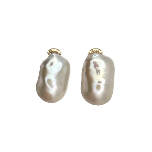 Pair of pearl earrings on a clear stand against a light gray background