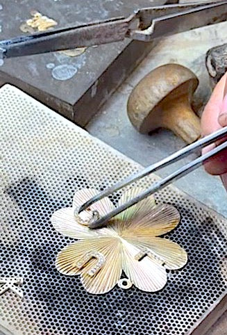 Gold jewelry being worked on with tweezers and a metal surface