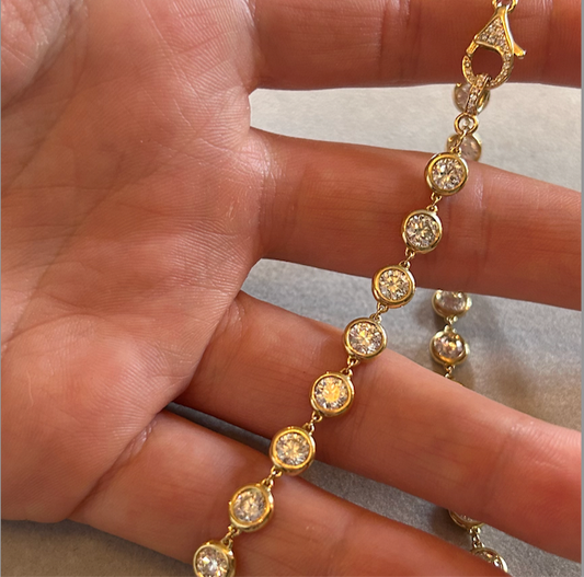 Gold necklace with diamonds held between fingers on a neutral background