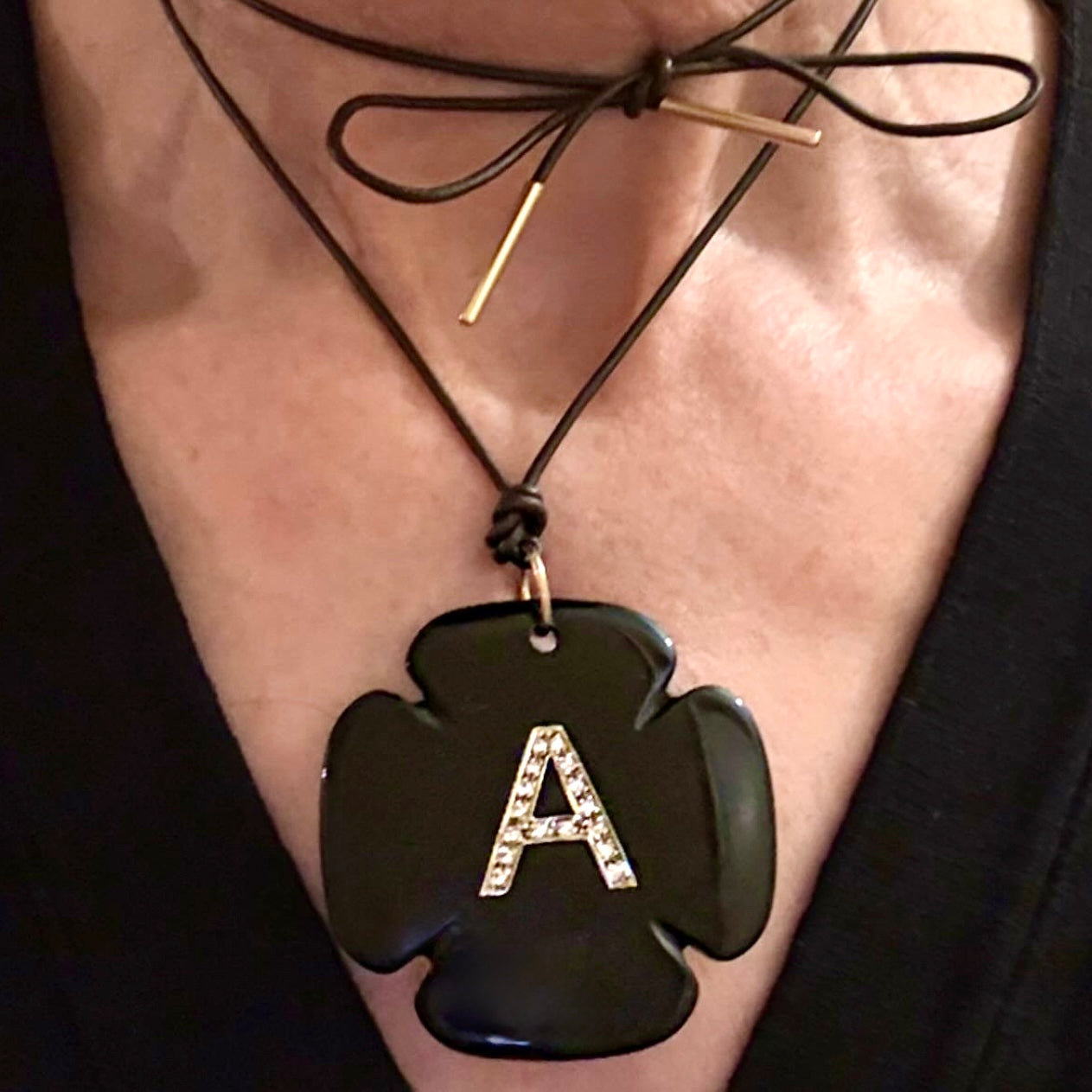 Necklace with a black cross-shaped pendant and letter 'A' on a person's neck.