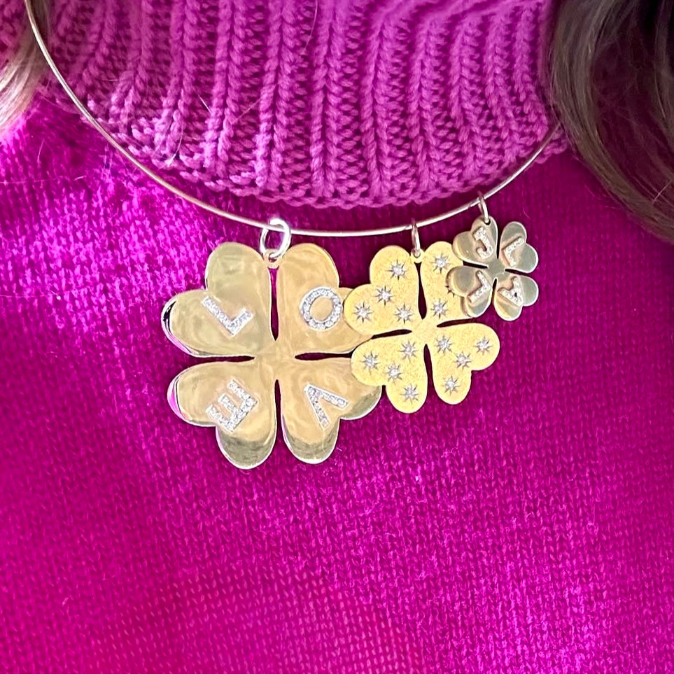 Gold necklace with floral design and 'LOVE' on a pink background
