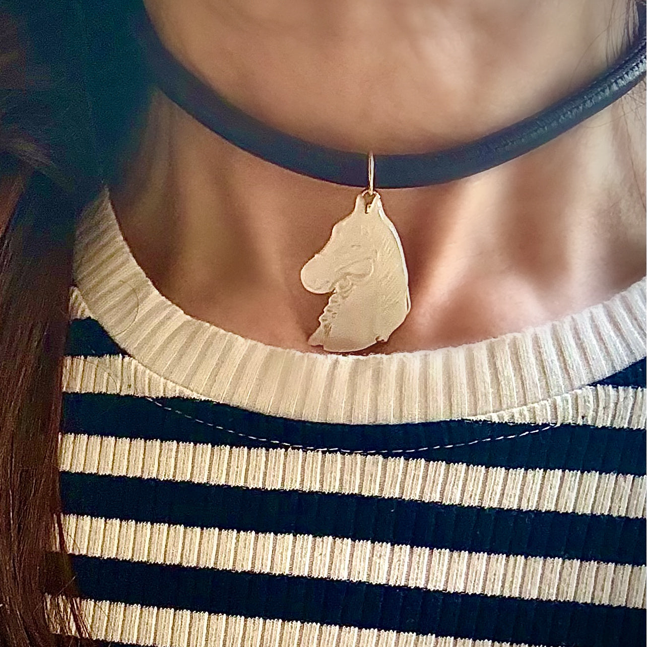 Person wearing a black choker with a horse pendant, striped shirt, and long hair.