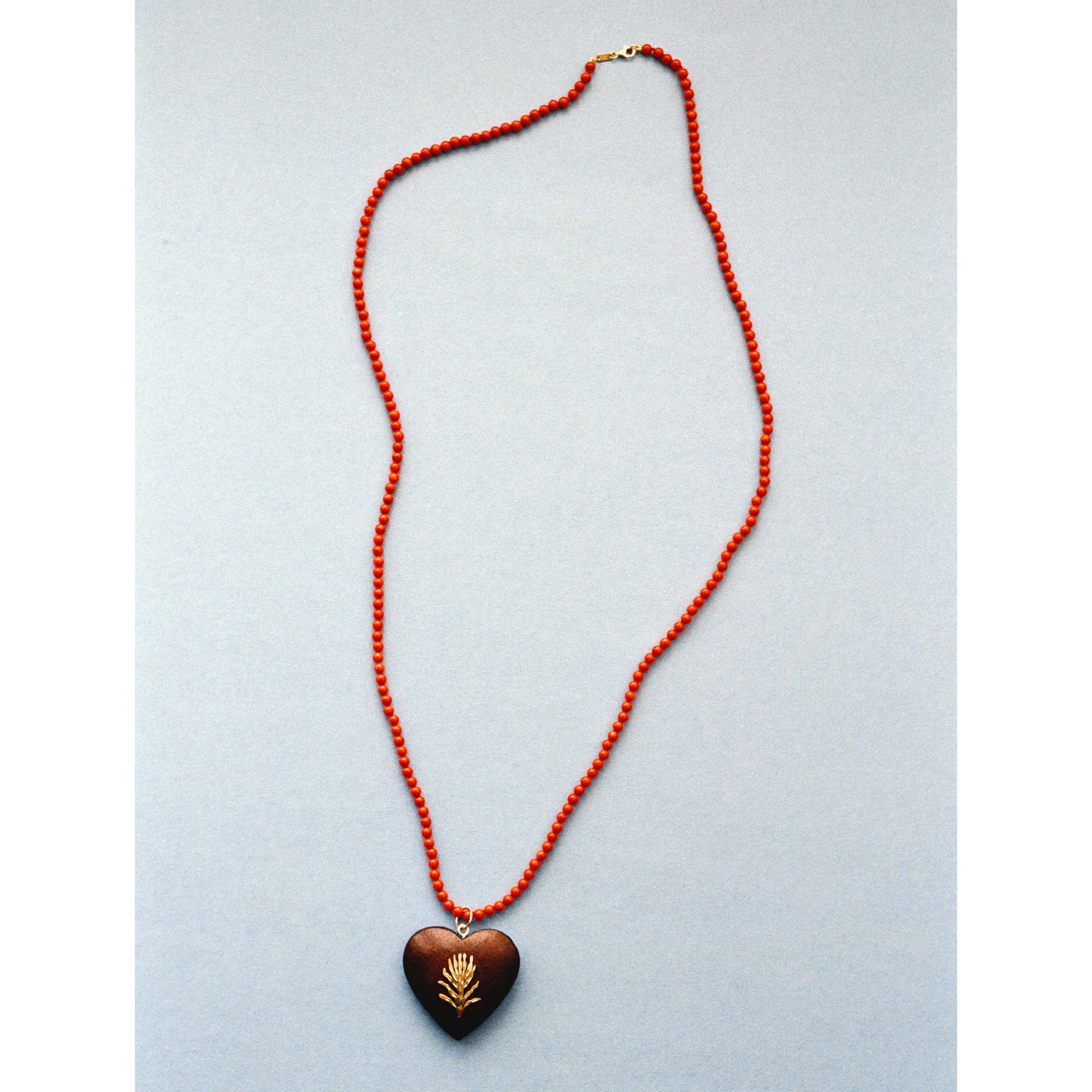 A heart-shaped wooden pendant necklace with a gold wheat design, suspended on a red beaded chain against a light gray background.