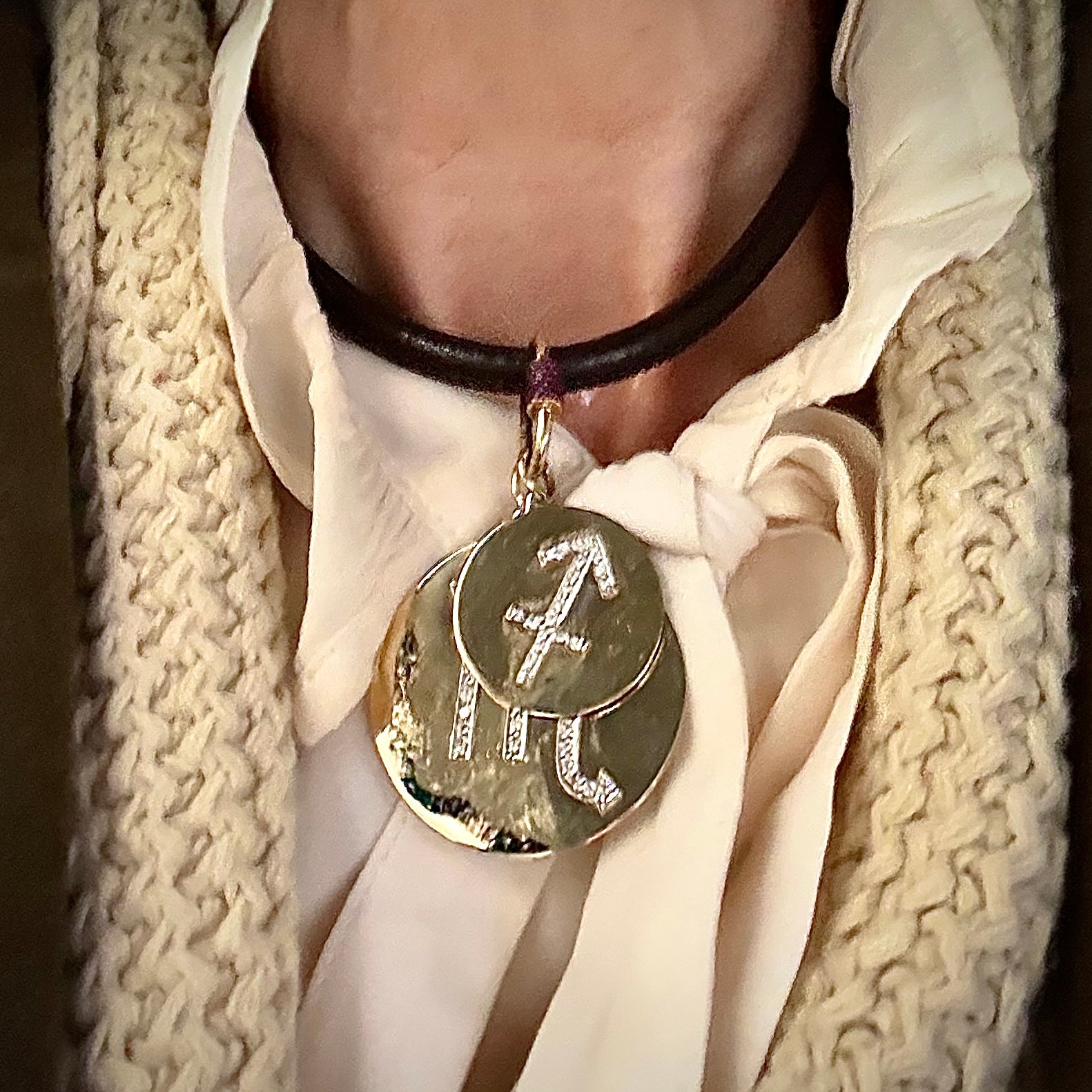 Necklace with two layered round pendants featuring Sagittarius and Scorpio symbols worn by a person in a white shirt and beige scarf.