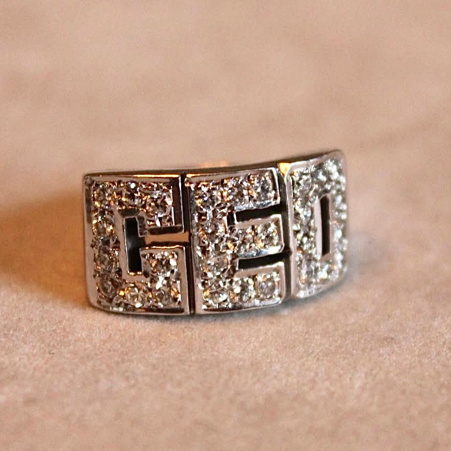 Silver ring with block letters in gemstones on a beige background