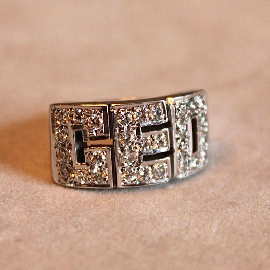 Silver ring with block letters in gemstones on a beige background