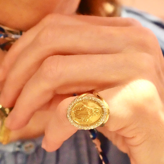Close-up of a hand wearing a gold ring with a religious design.