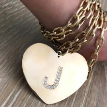 A gold heart-shaped pendant with a diamond pave initial 'J' on a gold chain.