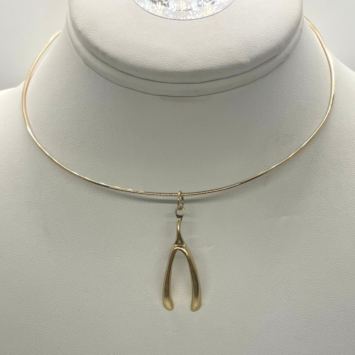 A gold-colored wishbone pendant displayed on a white mannequin necklace.