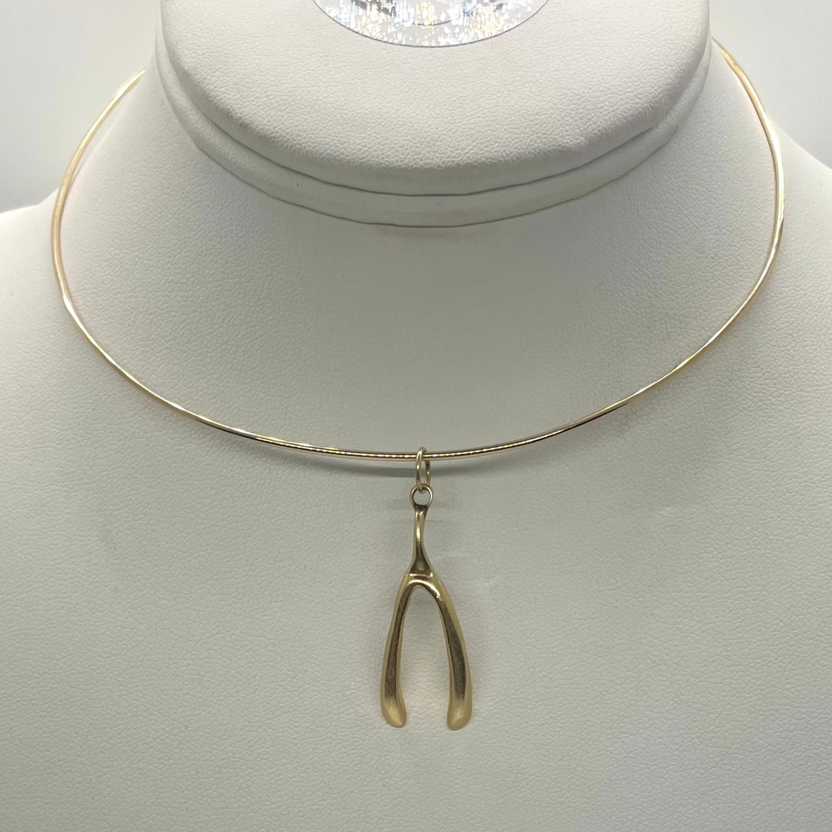 A gold-colored wishbone pendant displayed on a white mannequin necklace.