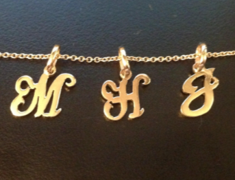 Gold necklaces with 'M', 'H', and 'J' charms on a dark background